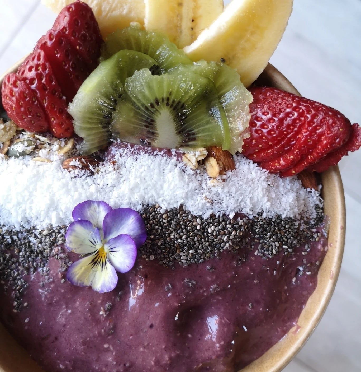 A berry smoothie bowl topped with strawberry, kiwi, banana, coconut and chia