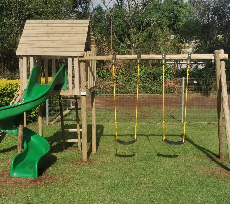 A wooden jungle gym with a slide and swings on the grass